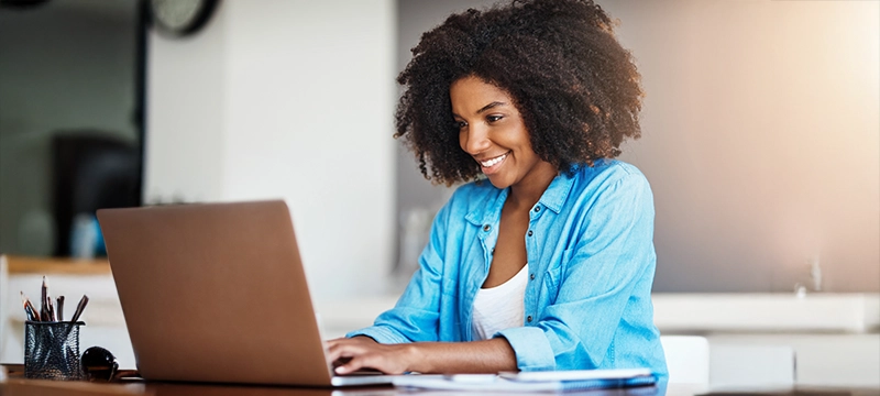 A smiling school psychologist typing on her laptop in a bright work setting