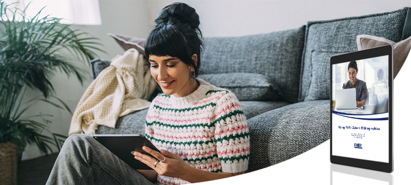 A woman smiles while sitting against her couch reading from a tablet, a graphic of the Zotero Bibliographies white paper sits in the foreground to represent that this is what the woman is reading or using